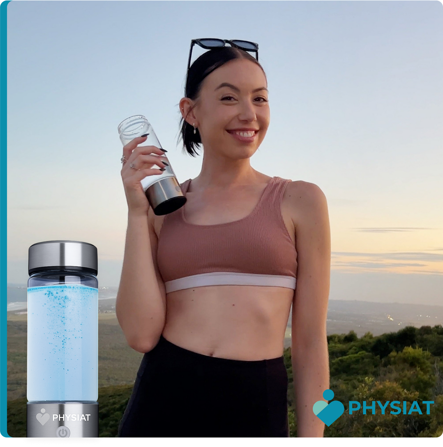 A smiling young woman in athletic wear holding a clear glass water bottle. She is standing outdoors against a scenic mountain landscape at sunset. In the foreground, a second PHYSIAT hydrogen water bottle is shown filled with active blue bubbles.